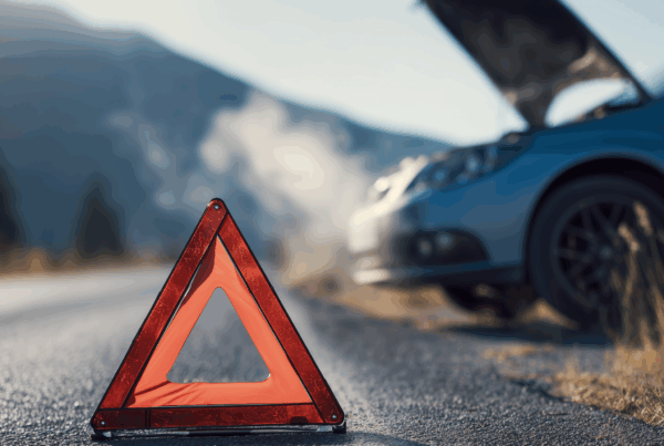 A close up of a warning triangle as a car sits with its hood open in the background